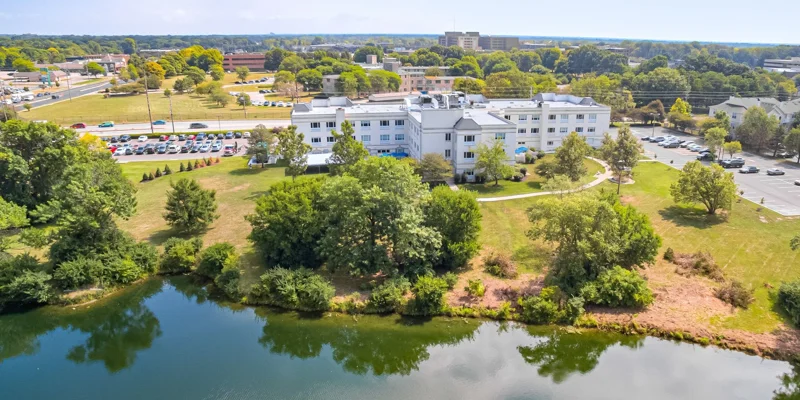 Aerial view of a serene recovery center surrounded by lush greenery and a peaceful lake, offering a tranquil environment for healing.