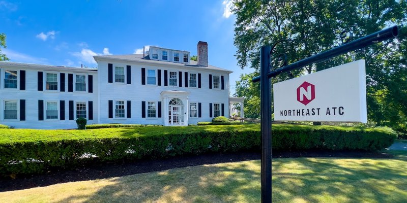 A beautiful, classic white building surrounded by well-maintained greenery. The Northeast ATC sign adds a welcoming touch under a bright blue sky.