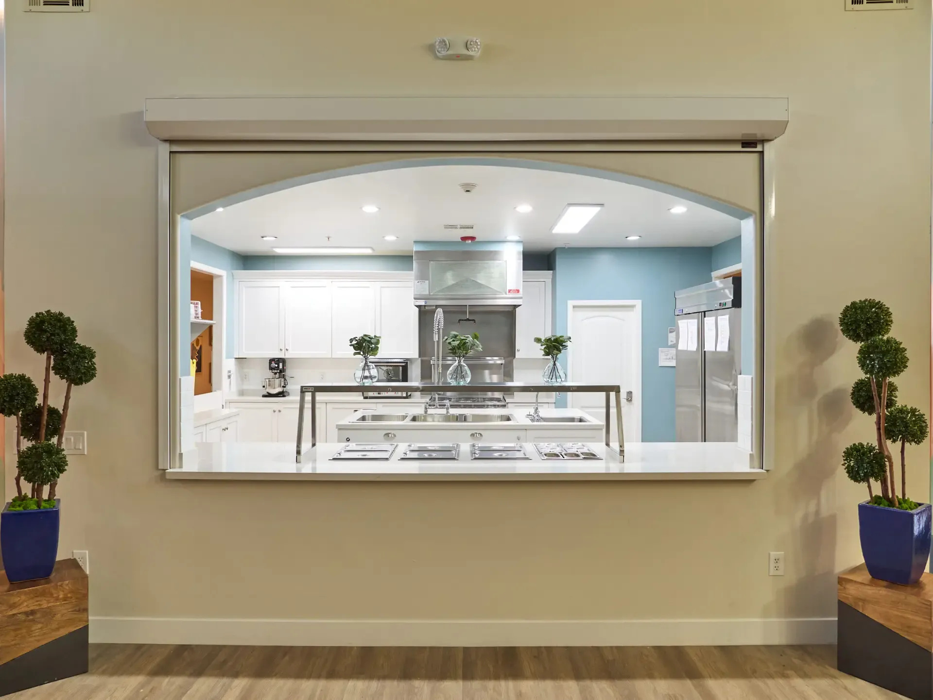 Modern kitchen viewed through large serving window with stainless appliances.
