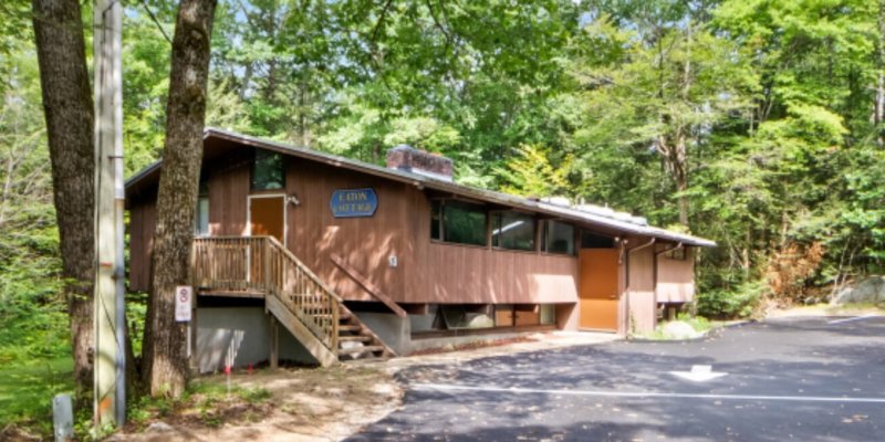 A rustic, elevated building surrounded by lush green trees, offering a quiet and secluded environment with a newly paved driveway.