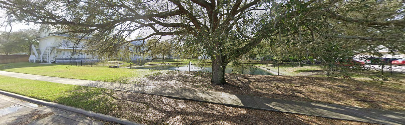Shaded yard with large tree and fenced pond near residential building