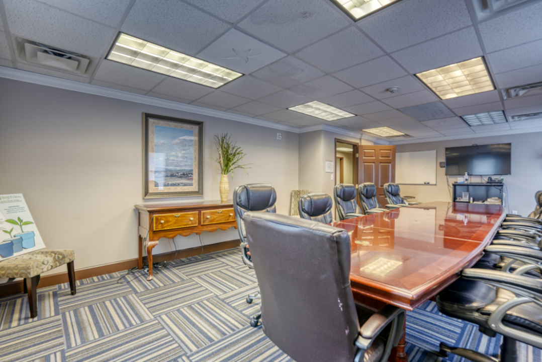 BrightView Health group room with large conference table, black office chairs, television, whiteboard, and blue patterned carpet
