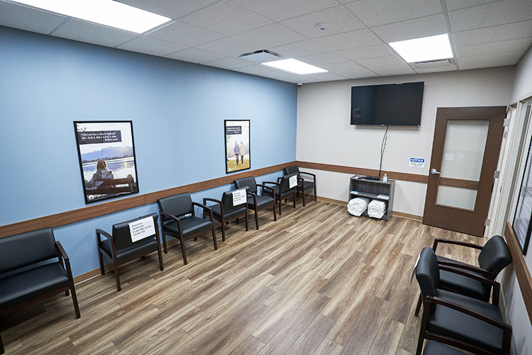 BrightView Health Marion treatment room with black patient chairs arranged along blue accent walls, wall-mounted television, recovery artwork, and wood-look flooring