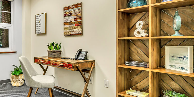 A cozy and organized office space with a simple desk, comfortable chair, and bookshelf featuring decorative items, creating a welcoming vibe.