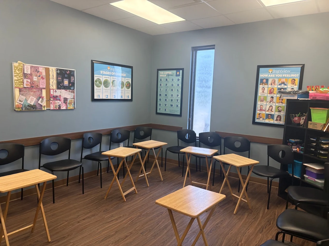 BrightView Akron group activity room with chairs, individual tables, recovery education posters, storage shelves, and wood-look flooring