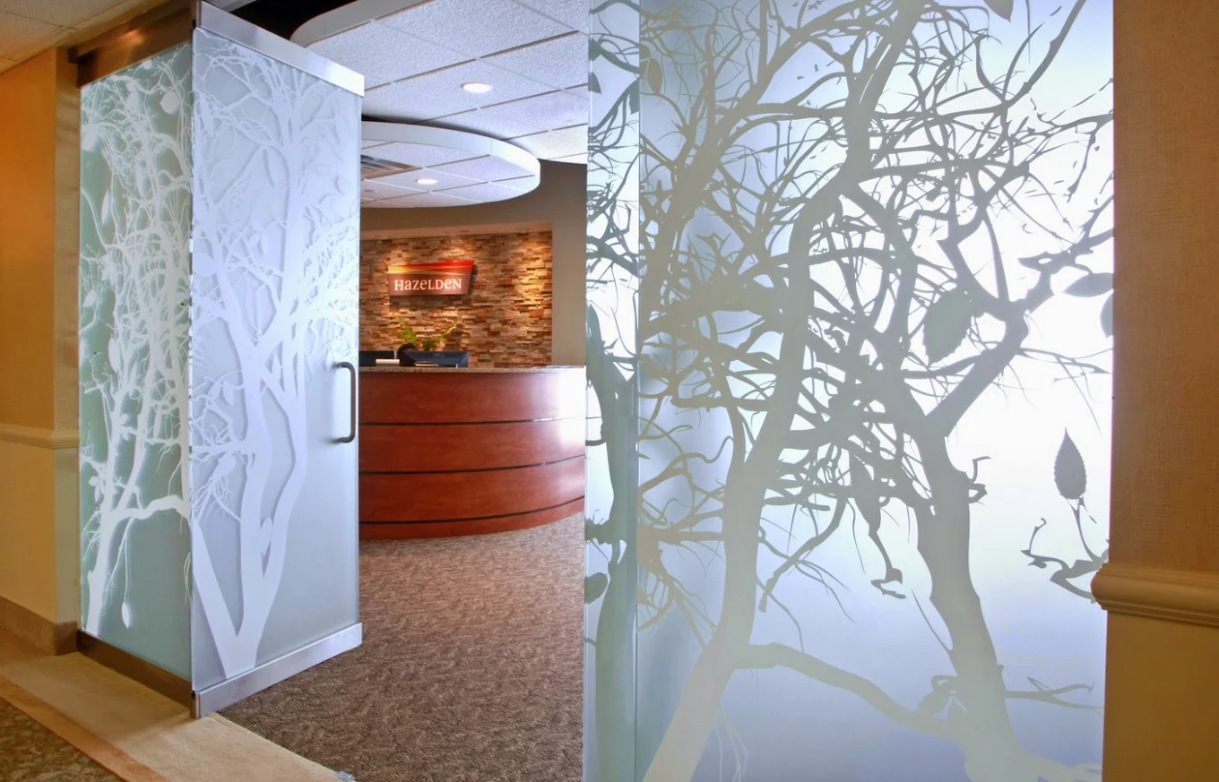 Hazelden reception entrance with decorative frosted glass panels featuring tree designs and a curved wood reception desk