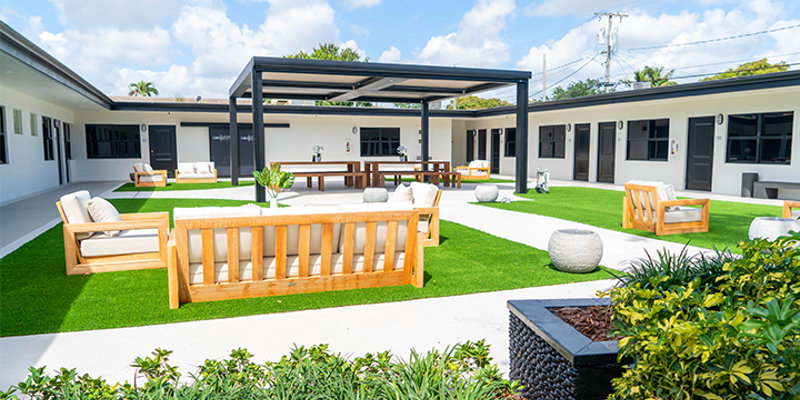  A bright, spacious courtyard with modern outdoor furniture, green lawns, and a shaded seating area, creating a serene environment for relaxation.