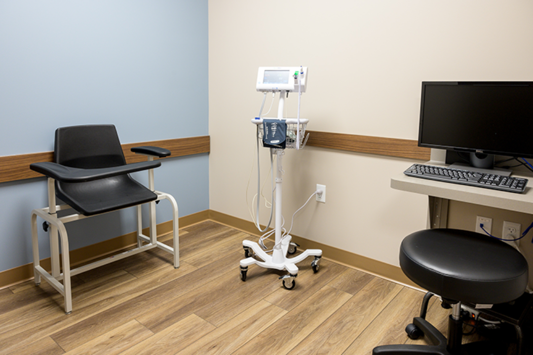 Clinical room with patient chair, vital-sign monitor, computer workstation, and medical stool