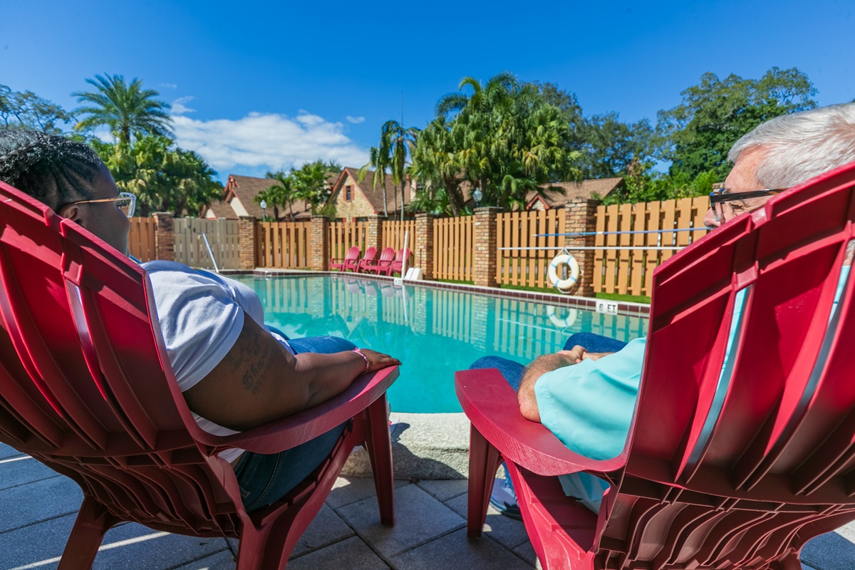 People relaxing in red chairs by the pool on a sunny day