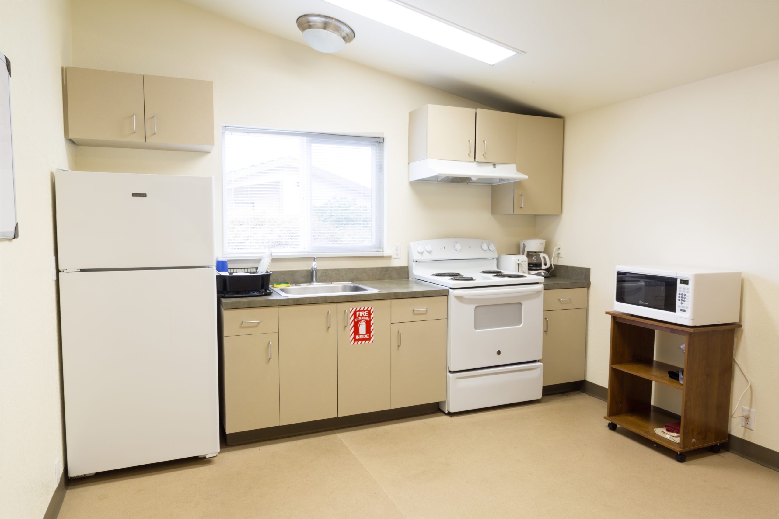 A small kitchen with beige cabinets, a stove, microwave, and fridge.