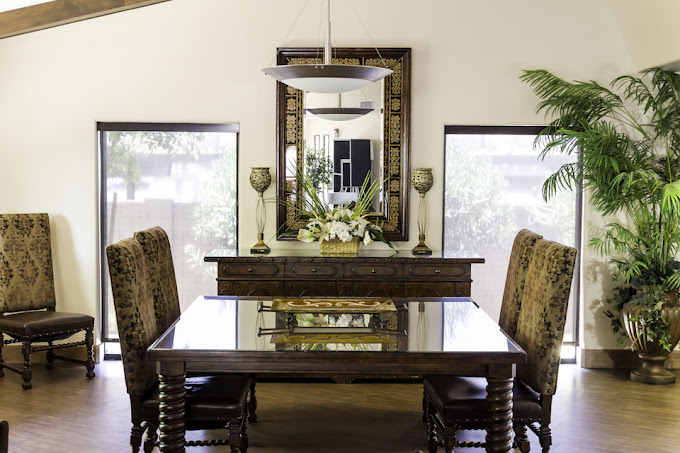 Dinning room with a plant, long table and large windows.