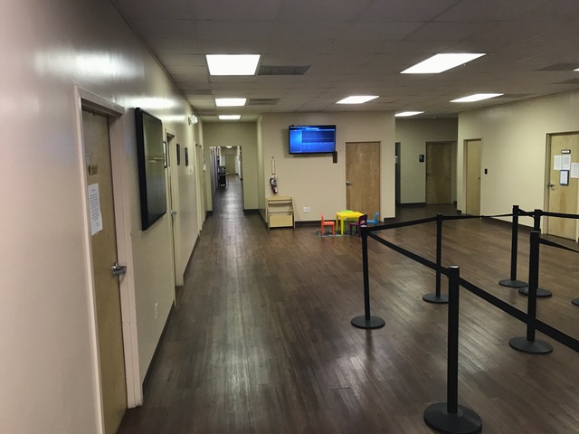 Interior hallway with wooden flooring, doors, a TV, and a waiting area.