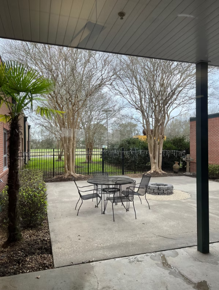 Outdoor seating area with black metal chairs and a firepit surrounded by trees and brick buildings