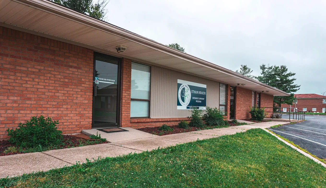 Front view of the clinic's brick building with sidewalk, lawn, signage, and adjacent parking area
