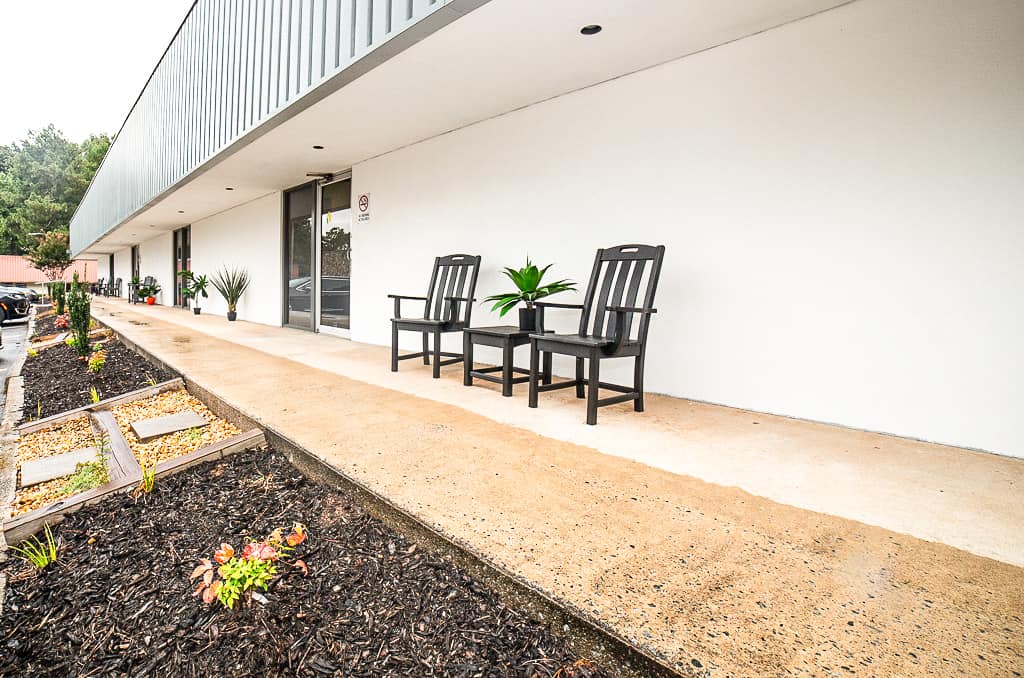 Outdoor seating area with two black chairs and a small table in front of a white building.