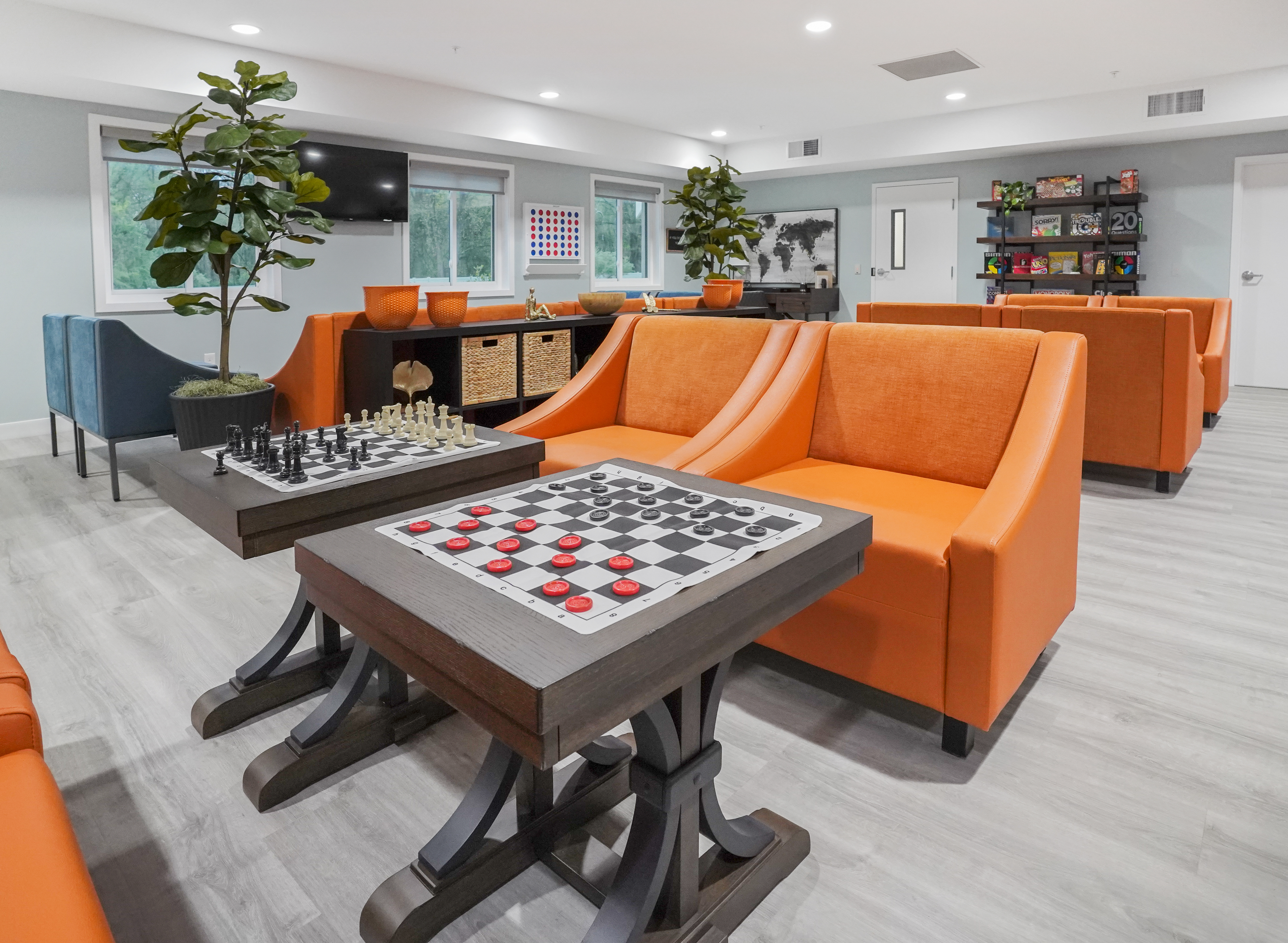 Bright lounge with games, orange chairs, and board-game tables.