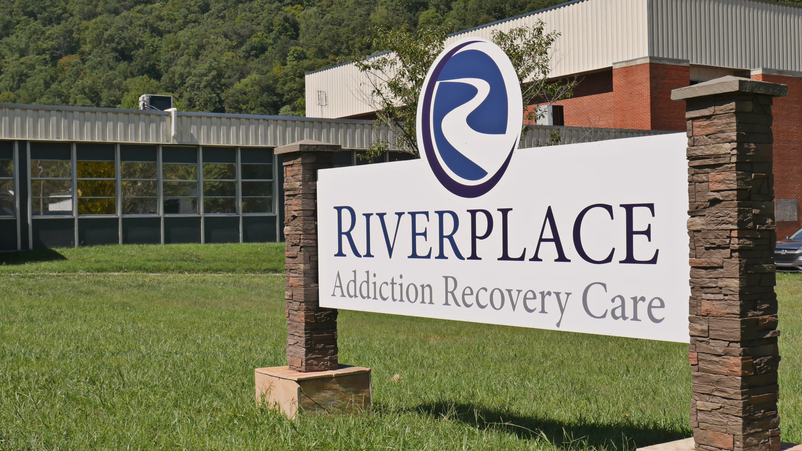 River Place sign on lawn with building and forest in background