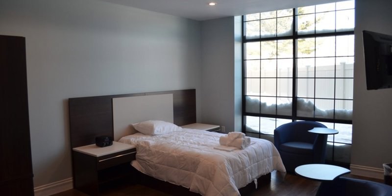 A modern, minimalist bedroom with a cozy bed, sleek furniture, and large windows offering natural light and a calming atmosphere.