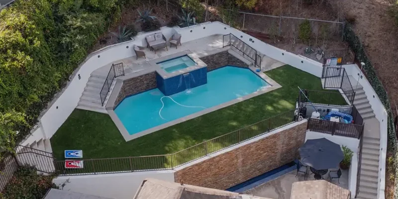 A well-designed backyard pool area with a spa, surrounded by lush greenery, tiered seating, and cozy seating arrangements on all levels.