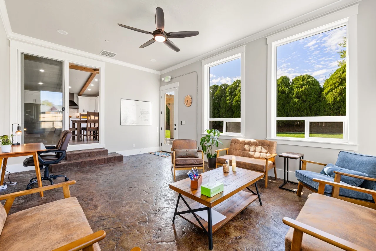 Communal room with chairs, tables, desk, and large windows