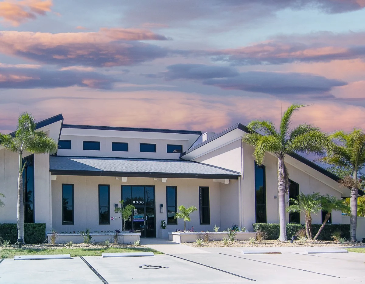 Modern rehab facility exterior with palm trees and sunset sky