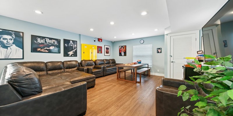 A spacious, modern lounge with comfortable leather seating, vibrant artwork, a game table, and plenty of natural light, creating a lively and welcoming atmosphere.