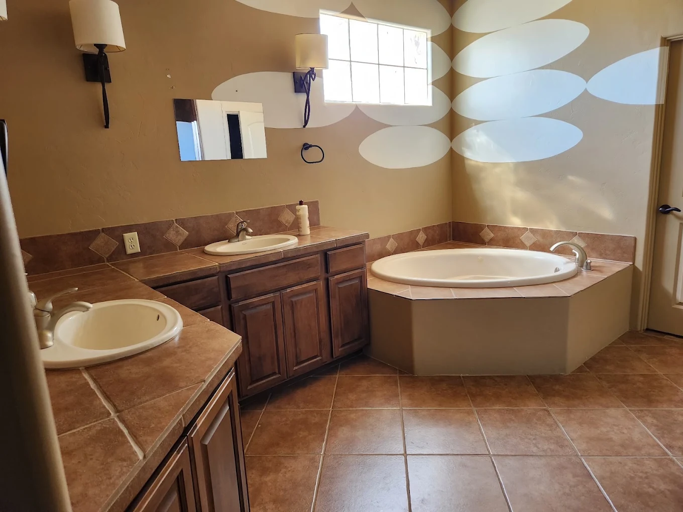 Spacious bathroom with dual sinks, wood cabinetry, tiled counters, and corner bathtub