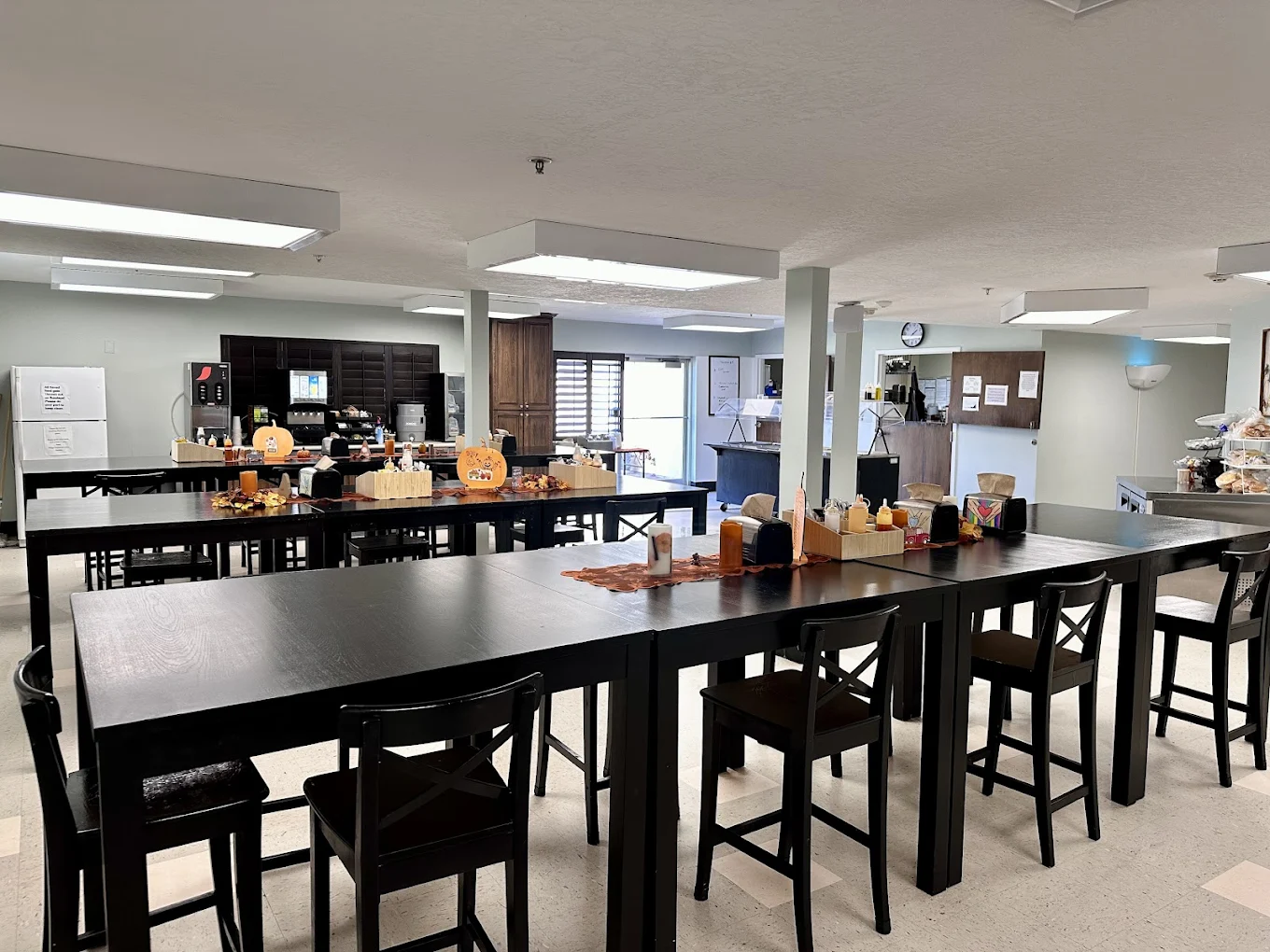 Large dining area with black tables, seasonal decorations, and self-serve beverage and food stations at New Roads Behavioral Health