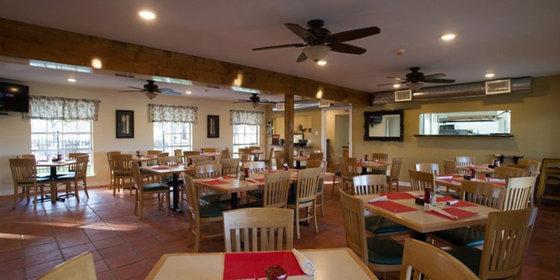 A warm, inviting dining area with cozy wooden tables and chairs, soft lighting, and ceiling fans, perfect for gathering and enjoying meals together.