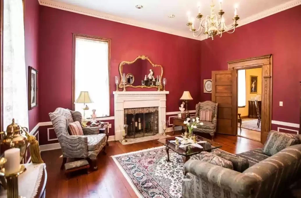 Elegant living room with red walls, fireplace, upholstered armchairs, chandelier, hardwood floors, and decorative area rug