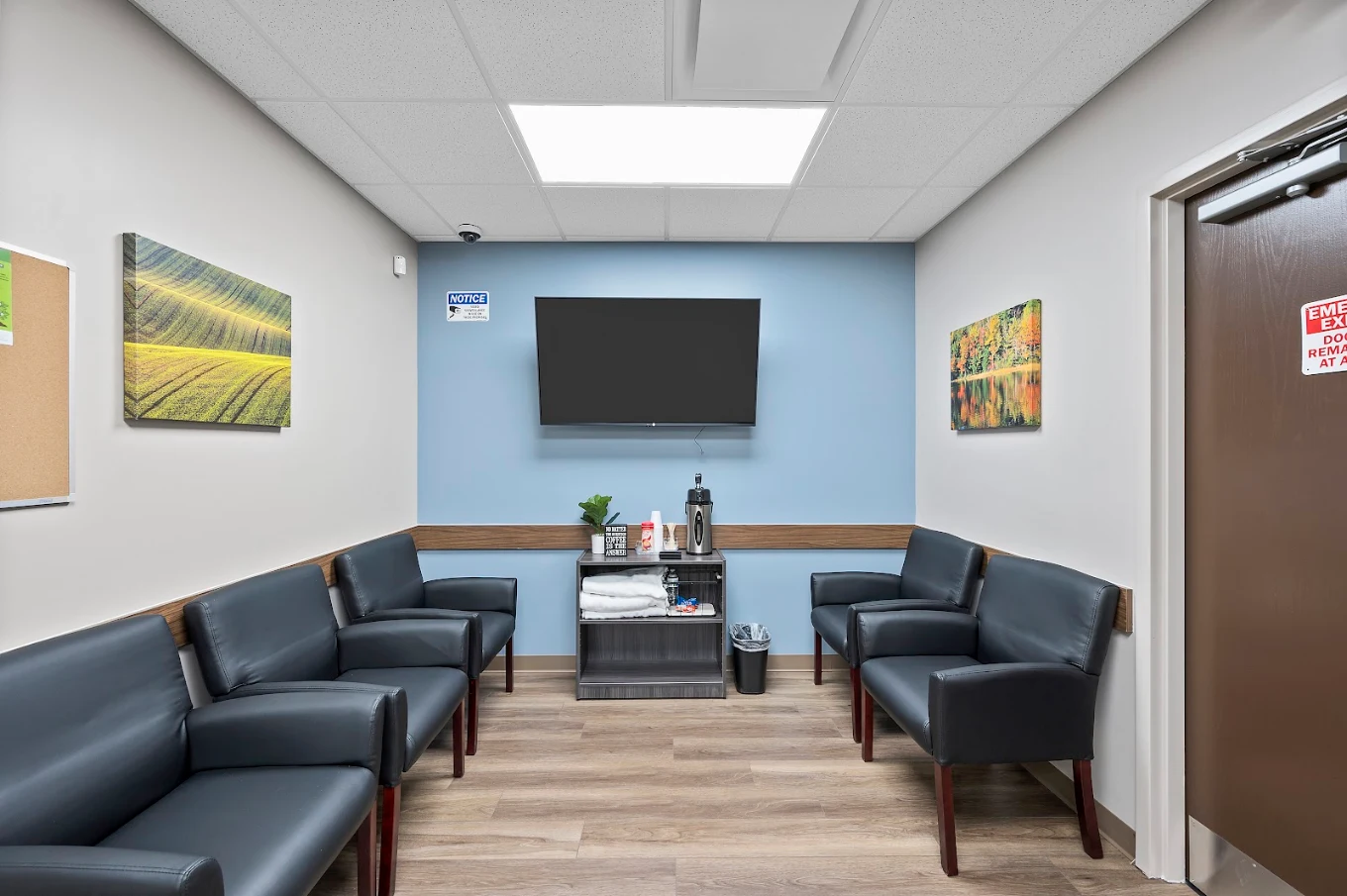Waiting room with black seating, television, and landscape artwork