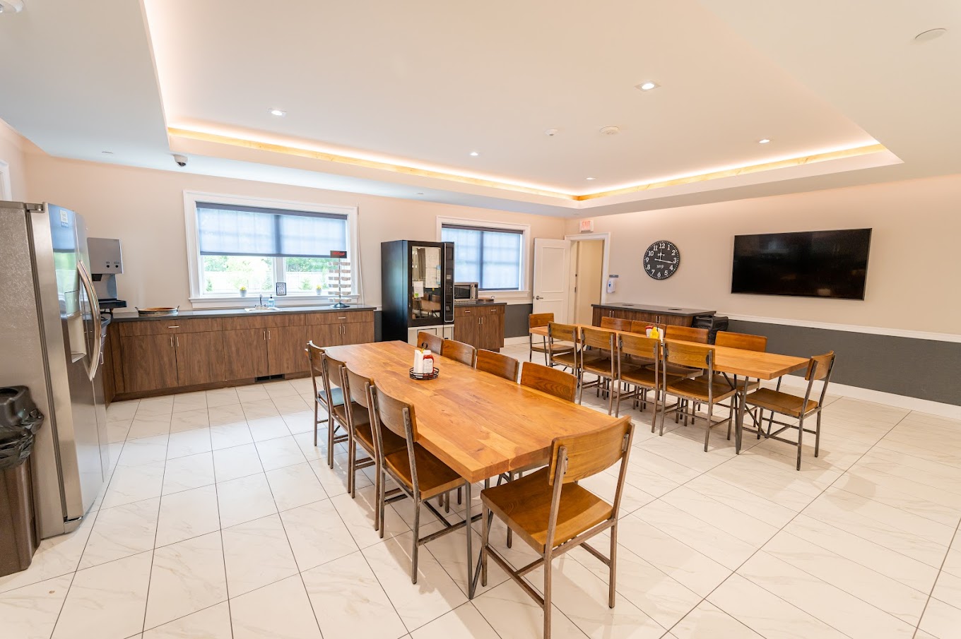  A modern dining area with wooden tables and chairs, stainless steel kitchen appliances, and a mounted TV, designed for communal meals.