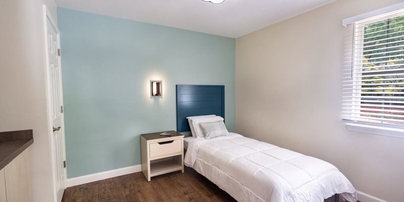 A serene and inviting bedroom featuring a cozy single bed with crisp white linens, a bedside table, and soft, calming blue accents.