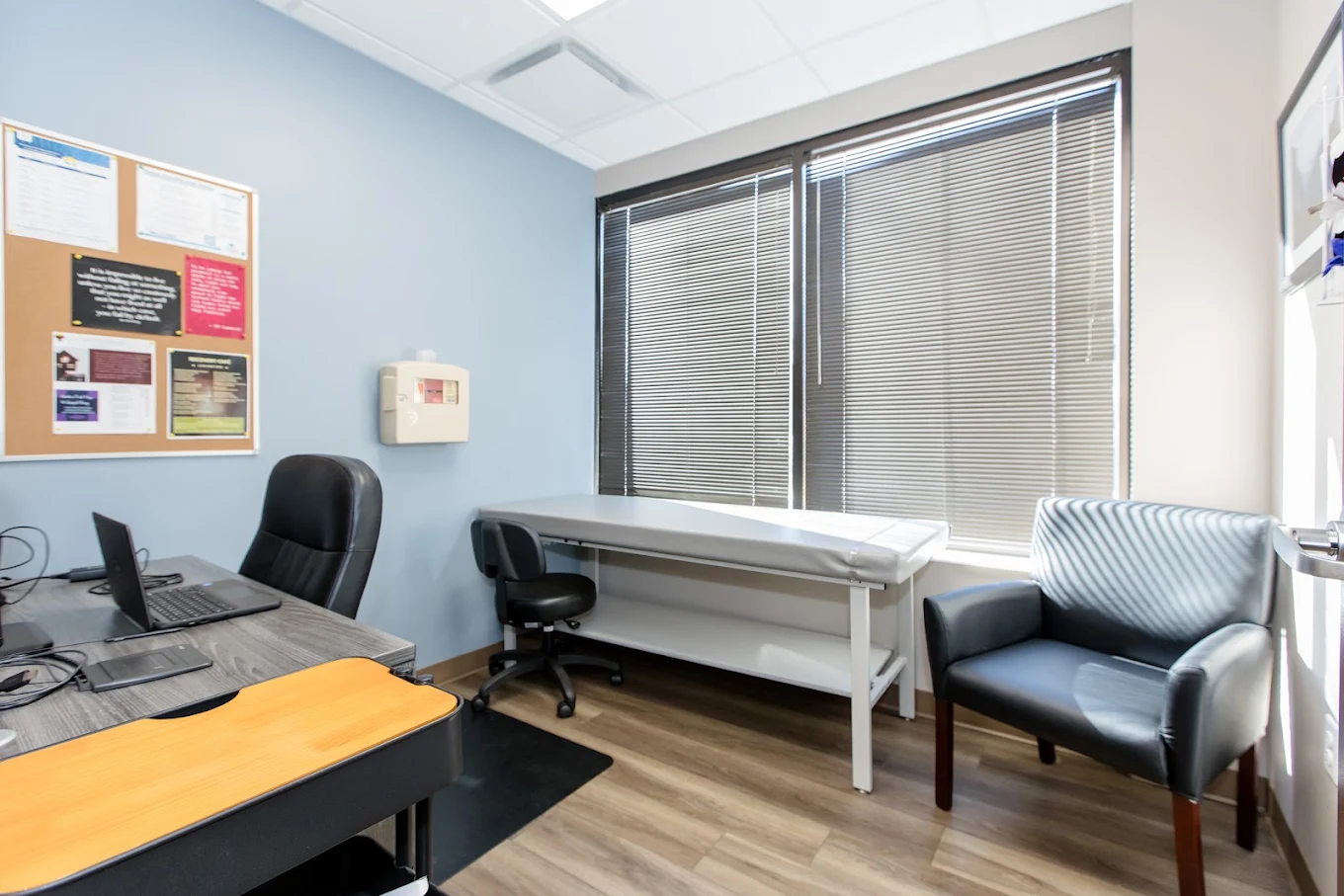 Clinical room with exam table, desk, laptop, and patient chair