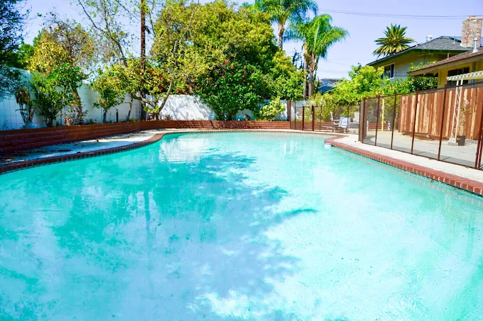 Large outdoor pool with safety fence and tropical trees