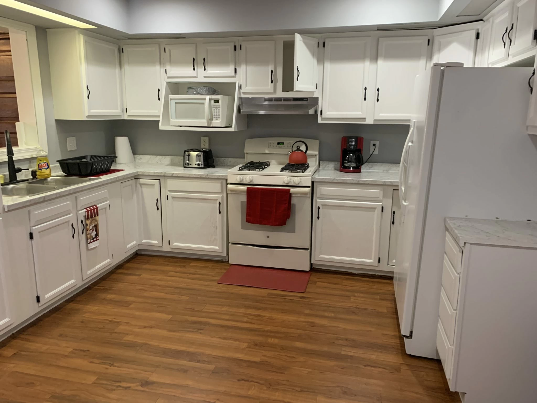 Spacious white kitchen with wood floor and red accents