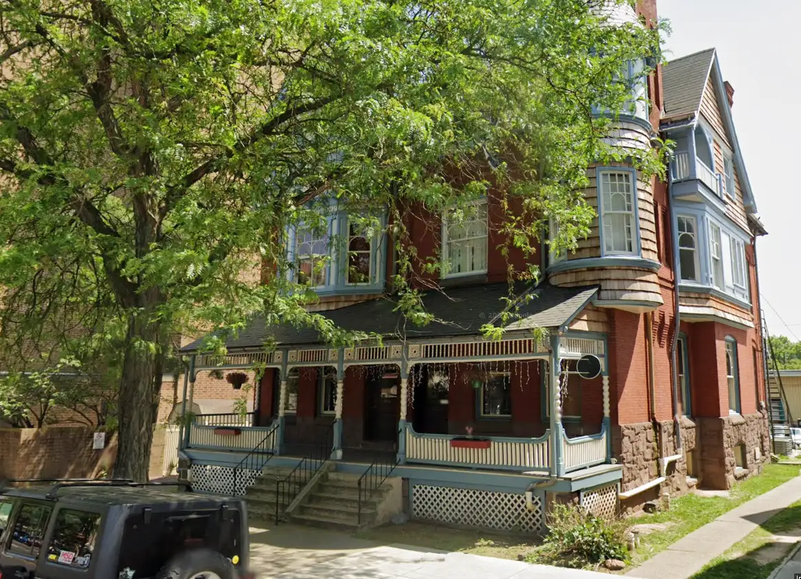 Brick rehab center with wraparound porch and large trees out front