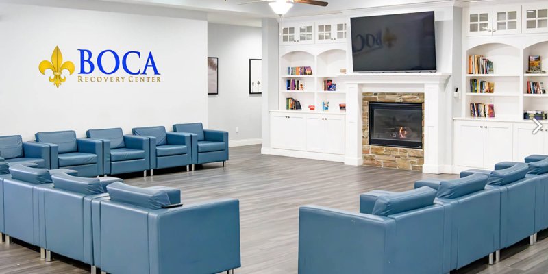 Bright, modern lounge area at Boca Recovery Center with comfortable blue seating, a cozy fireplace, bookshelves, and a large TV.