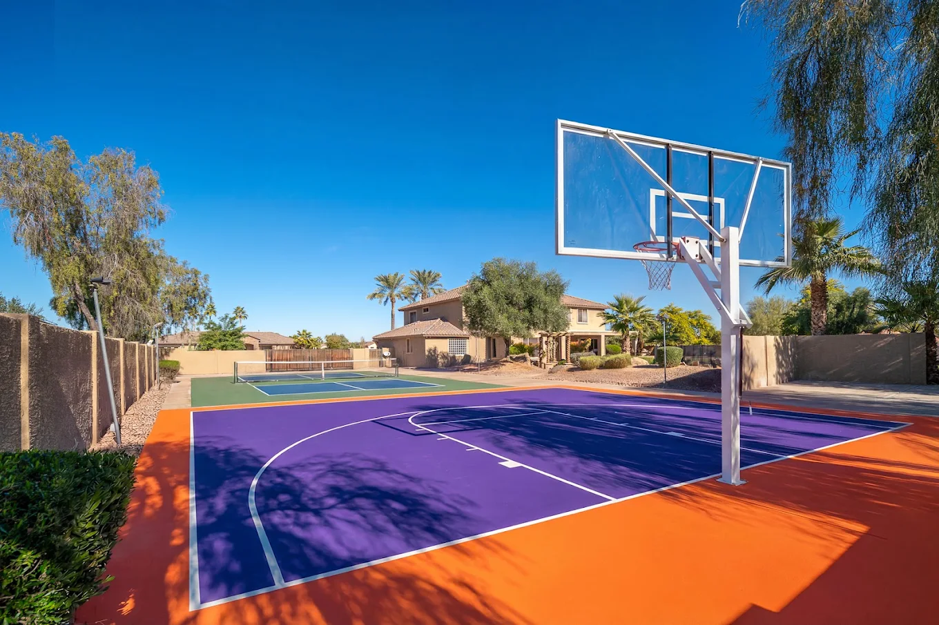 Outdoor basketball court beside a pickleball court on landscaped residential grounds