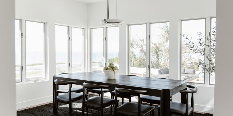 Elegant dining room with panoramic ocean views, featuring a sleek dark wood table, modern black chairs, and abundant natural light.