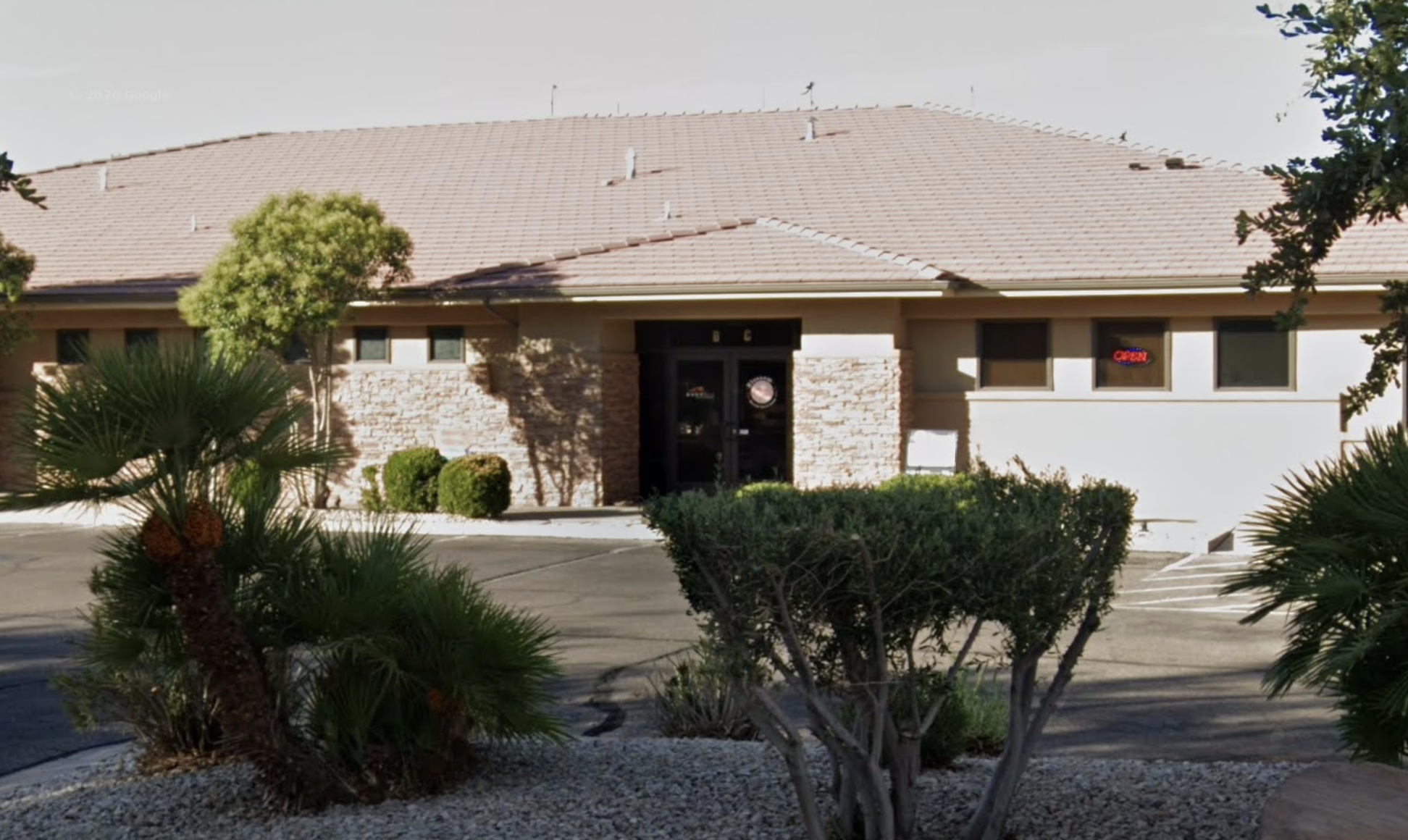 Single-story beige building with palm trees and shrubs