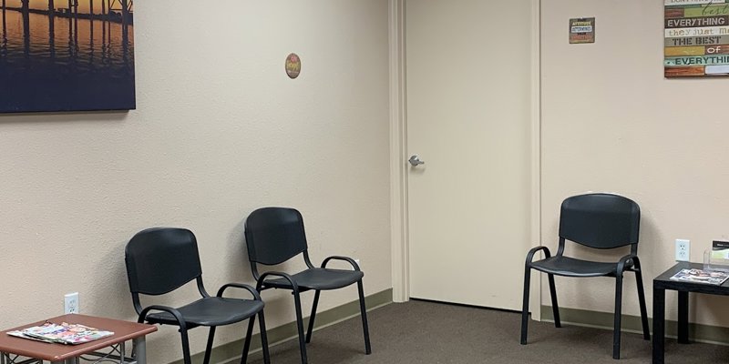 A quiet waiting room with simple black chairs, soft beige walls, and calming artwork, offering a welcoming and peaceful environment.