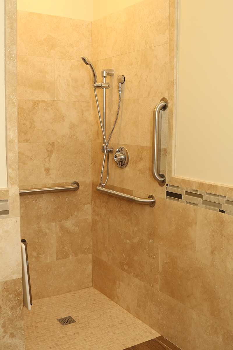 Tan-tiled shower with grab bars and handheld showerhead