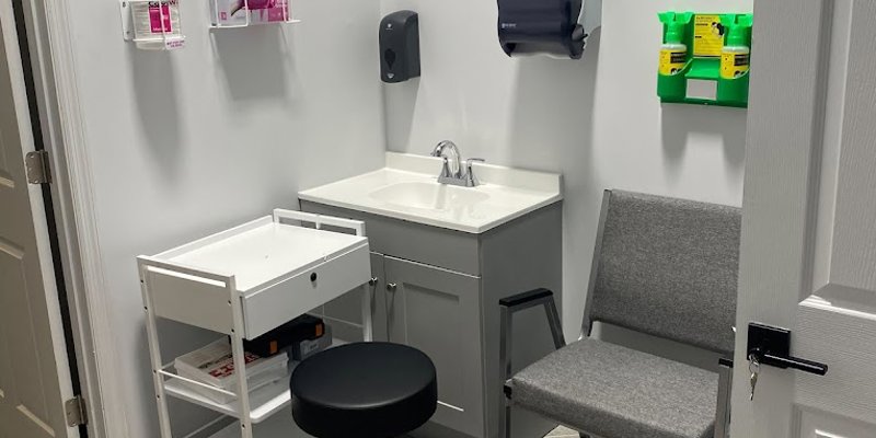 A clean, well-organized medical examination room with a chair, sink, and essential supplies, creating a comfortable and professional setting for care.