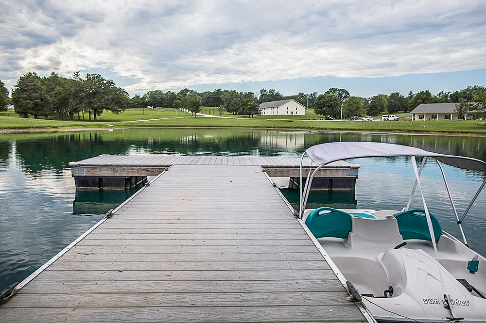 A dock extending over a lake with a paddle boat tied to it.