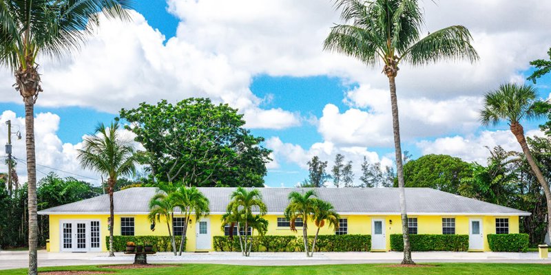 Yellow rehab facility with palm trees and lawn.