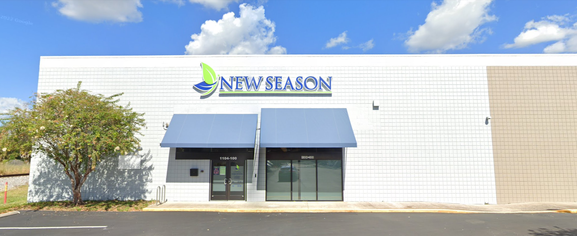 Exterior of a white rehab facility with blue awnings and a "New Season" sign.