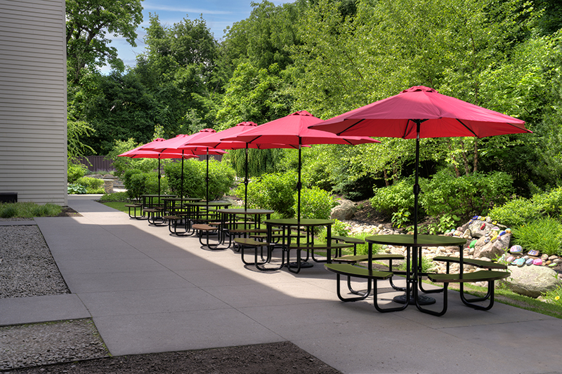 Patio tables with red umbrellas beside landscaped grounds