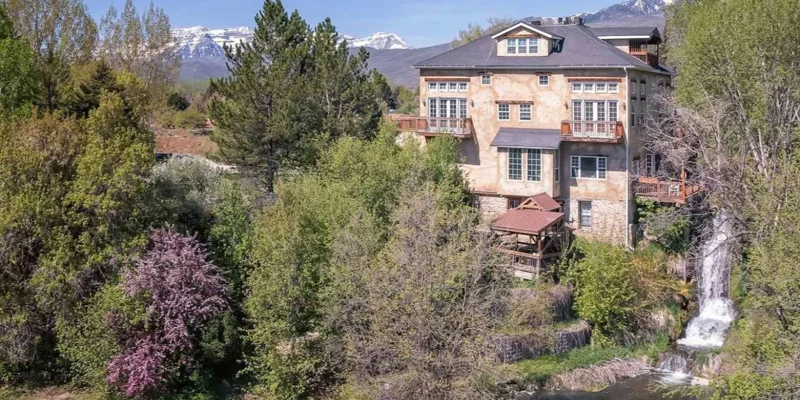 A charming hillside estate surrounded by lush greenery, blooming trees, and a cascading waterfall, with snow-capped mountains in the distance. Peaceful and picturesque.