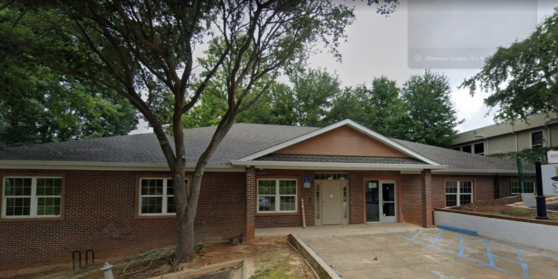 A welcoming brick building surrounded by greenery, featuring a sign for New Season Treatment Center, with accessible parking and entryway.